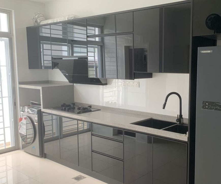 A long galley kitchen with grey gloss doors and black trim, a sink under the window, cooker hood, washing machine and a dark fridge.