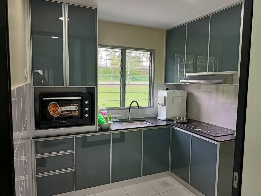 A grey-green kitchen with a microwave niche, a water dispenser and a window over the sink.